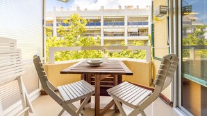 A balcony with a table and two chairs, a view of a building with balconies, and a window with blinds. - Nice apartment for 2 guests with A/C, pool (Salou)
