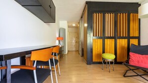 A modern room with a wooden floor, a desk with two chairs, a small stool, and a bed with a red pillow. - Nice apartment for 2 guests with A/C, pool (Salou)