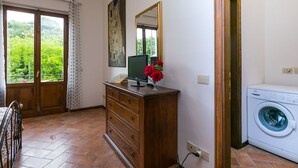 Une pièce comprenant une commode en bois, un ordinateur de bureau, un lave-linge et une grande fenêtre donnant sur un paysage verdoyant.