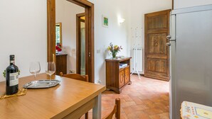 Un coin repas avec une table en bois, des chaises, une bouteille de vin et des verres. On y trouve également un réfrigérateur et un meuble sur lequel est posé un vase de fleurs.