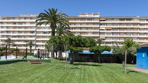 En hotelgård med swimmingpool, palmer og en blå bygning.