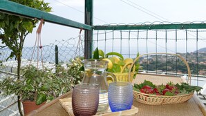 Ein Balkon mit Blick, mit einem Blumentopf, einer Glaskaraffe, einem Korbwägelchen mit Erdbeeren und zwei Gläsern.