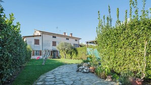 A stone pathway leading to a white building with brown shutters, surrounded by lush greenery and potted plants. - Beautiful apartment for 4 people with WIFI, A/C, TV, patio and pets allowed (Pietrasanta)