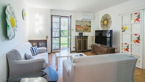 A living room with a sofa, a coffee table, and a TV. There is a door leading to a balcony. - Beautiful apartment for 4 people with WIFI, A/C, TV, patio and pets allowed (Pietrasanta)