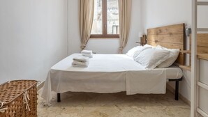 Une chambre à coucher comprenant un lit, une tête de lit en bois, une table de chevet, une lampe, une fenêtre avec des rideaux et un appareil de climatisation.
