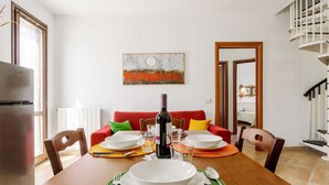 A dining area with a wooden table set for four, a red sofa, and a painting on the wall. - Lovely apartment for 6 people with A/C, WIFI, TV and terrace (San Vito Lo Capo)