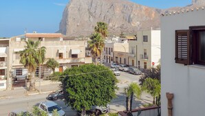 A residential street with buildings, cars, and a prominent mountain in the background. - Lovely apartment for 6 people with A/C, WIFI, TV and terrace (San Vito Lo Capo)