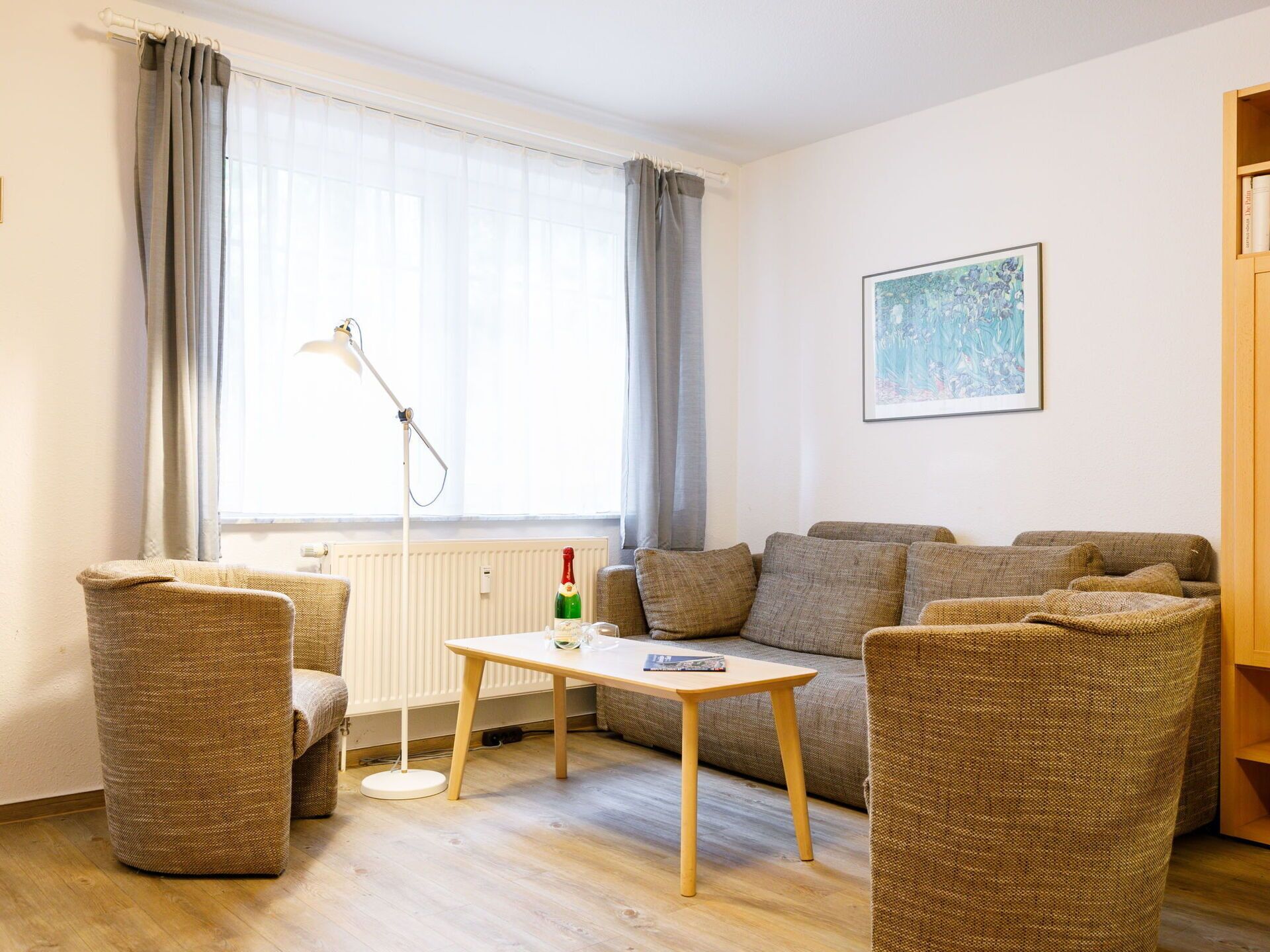 Een gezellige woonkamer met een bank, twee fauteuils, een kleine tafel, een vloerlamp en een radiator.
