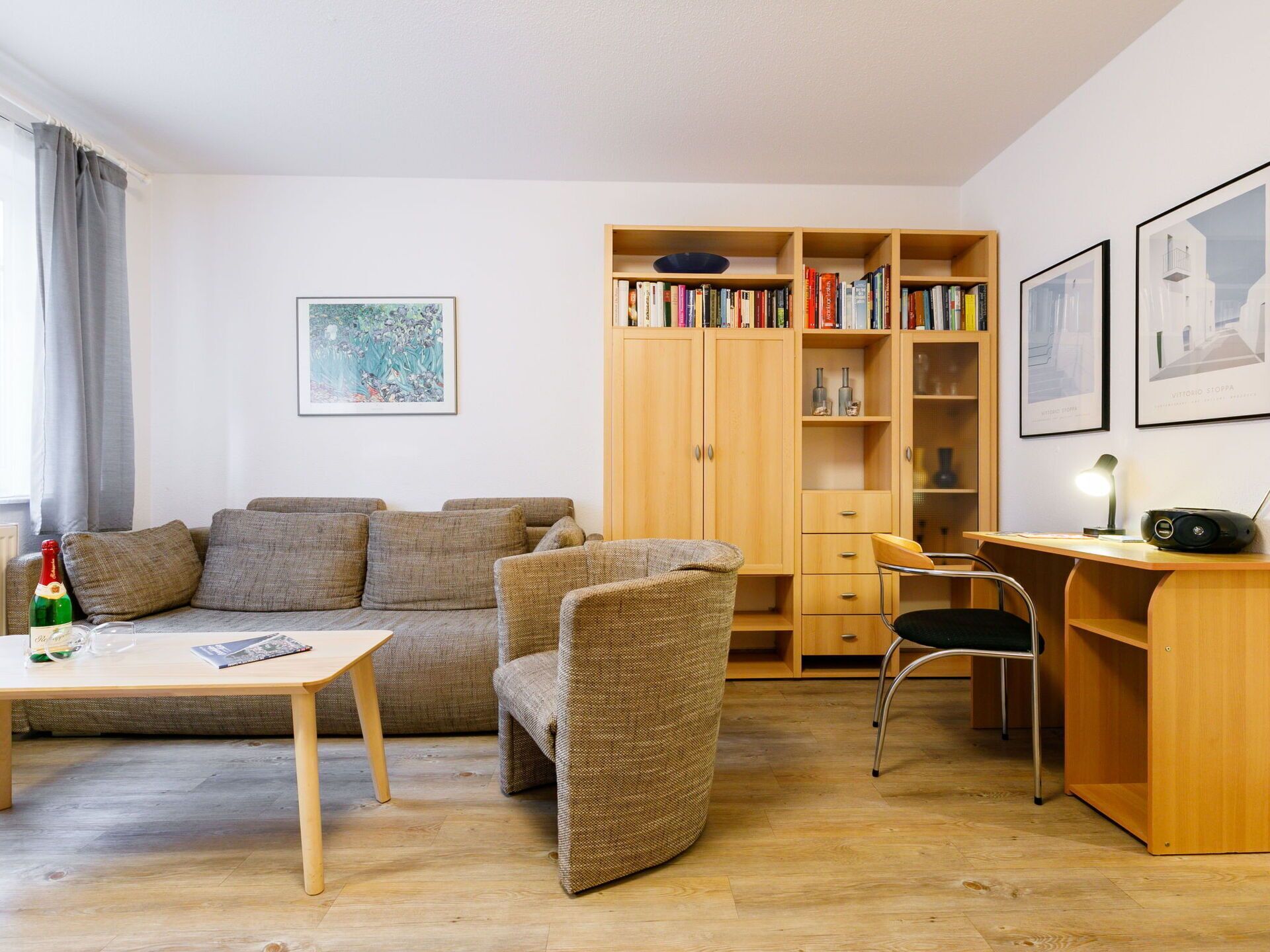 A cozy living room with a sofa, armchair, wooden desk, and bookshelf.