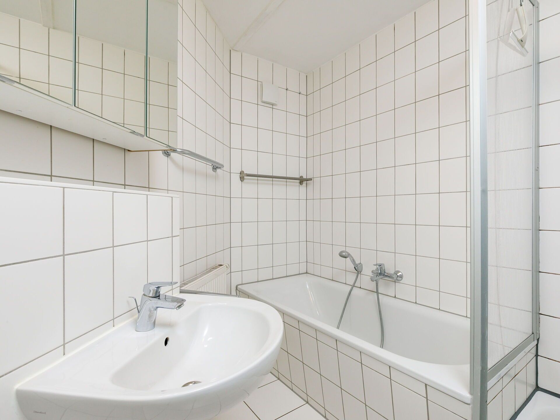 Ein Badezimmer mit weißen Fliesen, einem Waschbecken, einer Badewanne und einer Duschkabine aus Glas.