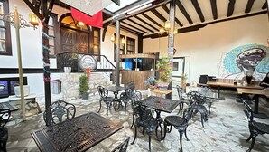 An outdoor seating area with tables and chairs, a stone floor, and a mural on the wall. - Kaleici Konak (Amasya)
