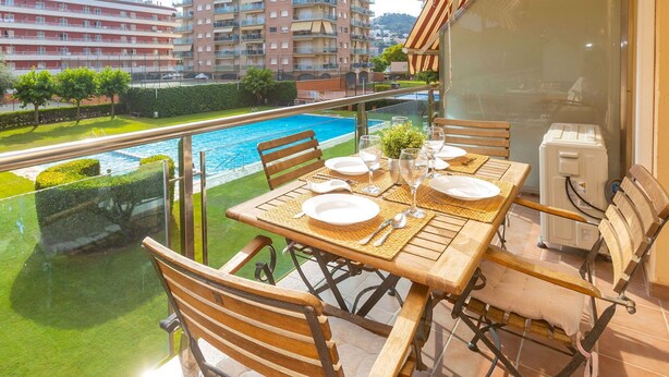 A balcony with a table set for dining, overlooking a swimming pool and a residential area. - Lovely apartment for 6 guests with pool, WIFI, A/C, TV, balcony and pets allowed (Santa Susanna)