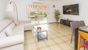 A living room with a sofa, a coffee table, a dining table with chairs, a potted plant, and a TV mounted on the wall. - Lovely apartment for 6 guests with pool, WIFI, A/C, TV, balcony and pets allowed (Santa Susanna)