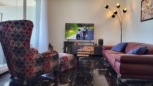 Una sala moderna con un televisor de pantalla plana grande, un sofá, un sillón estampado y una lámpara de pie.