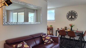Una sala moderna con un sofá de cuero, una mesa de comedor con sillas y un espejo grande con marco decorativo.