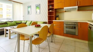 Une cuisine moderne avec des meubles en bois, un four encastré et un coin repas comprenant une table blanche et des chaises orange.