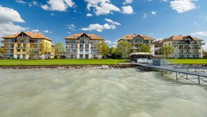 Une rangée d’immeubles à plusieurs étages dotés de balcons, une zone herbeuse et une rivière au premier plan.