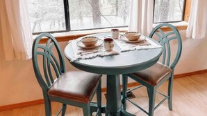 Ein runder Tisch mit vier Stühlen, ein Fenster mit Blick auf schneebedeckte Bäume und eine Tischdekoration mit Schüsseln und einer Tasse.