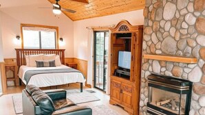 Ein Schlafzimmer mit Bett, Holz-Kopfteil, Kamin aus Stein und Fernseher in einem Holzkabinett.