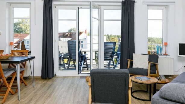 A modern living room with a sofa, chairs, a dining table, and a balcony with chairs. - Cosy apartment for 4 people with WIFI, TV, balcony and pets allowed (Wolgast)