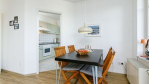 A modern kitchen with white cabinets, a dining table with chairs, and a pendant light. - Cosy apartment for 4 people with WIFI, TV, balcony and pets allowed (Wolgast)