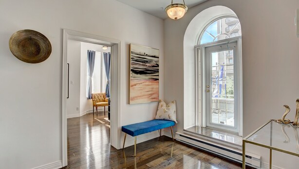 A hallway with a bench, a door, a wall-mounted artwork, and a window with a view of buildings.