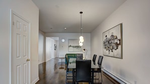 A dining area with a table and chairs, a pendant light, and a painting on the wall.