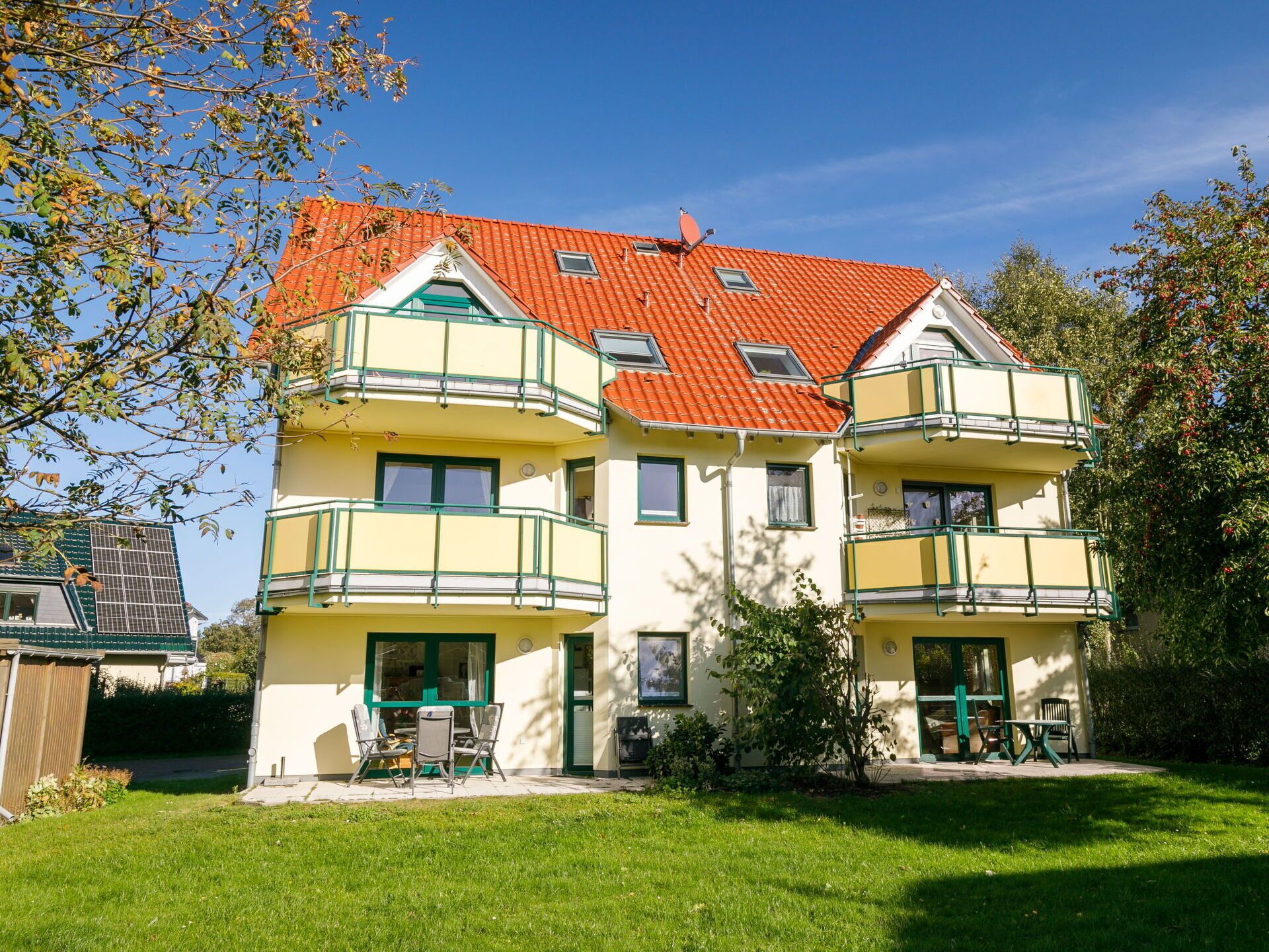 A multi-story building with a red-tiled roof, green balconies, and a well-maintained lawn.