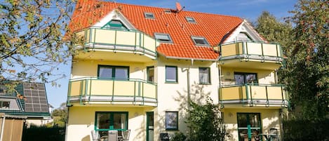 A multi-story building with a red-tiled roof, green balconies, and a well-maintained lawn.