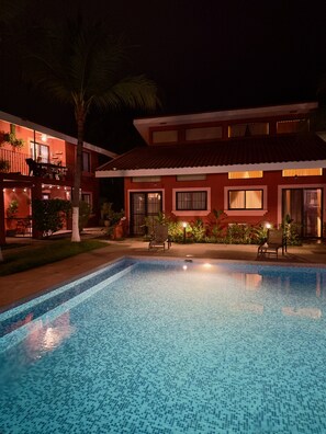 A swimming pool with a tiled deck, a two-story building with balconies, and a palm tree.