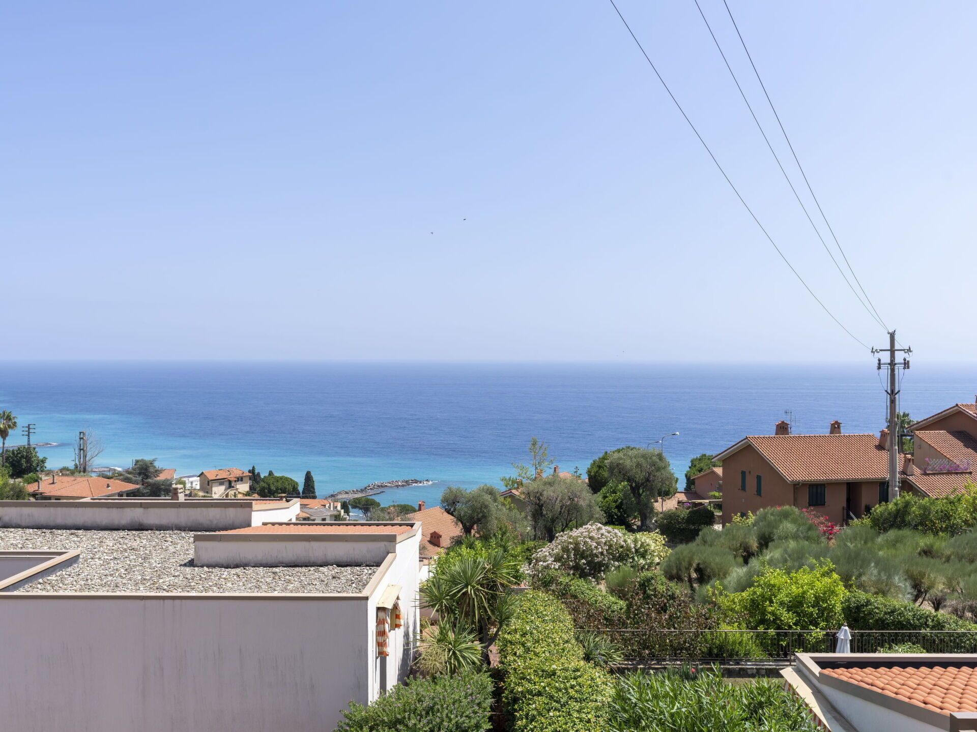Ein Küstenwohngebiet mit Häusern, freiem Blick auf das Meer und einer Stromleitung.