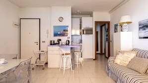 A compact living space with a kitchenette, a dining area with a table and chairs, and a sofa. - Nice apartment for 4 people with pool, A/C, WIFI, terrace and pets allowed (Bordighera)