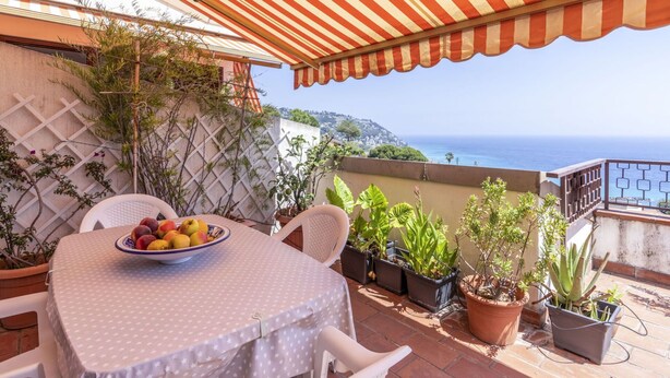 A patio with a round table, a bowl of fruit, potted plants, and a view of the sea. - Nice apartment for 4 people with pool, A/C, WIFI, terrace and pets allowed (Bordighera)