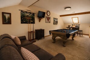 A room with a pool table, a brown leather couch, a television, and various wall art. - Cardinal's Nest • Sleeps 10 • Near Dollywood, Pigeon Forge & Gatlinburg (Sevierville)