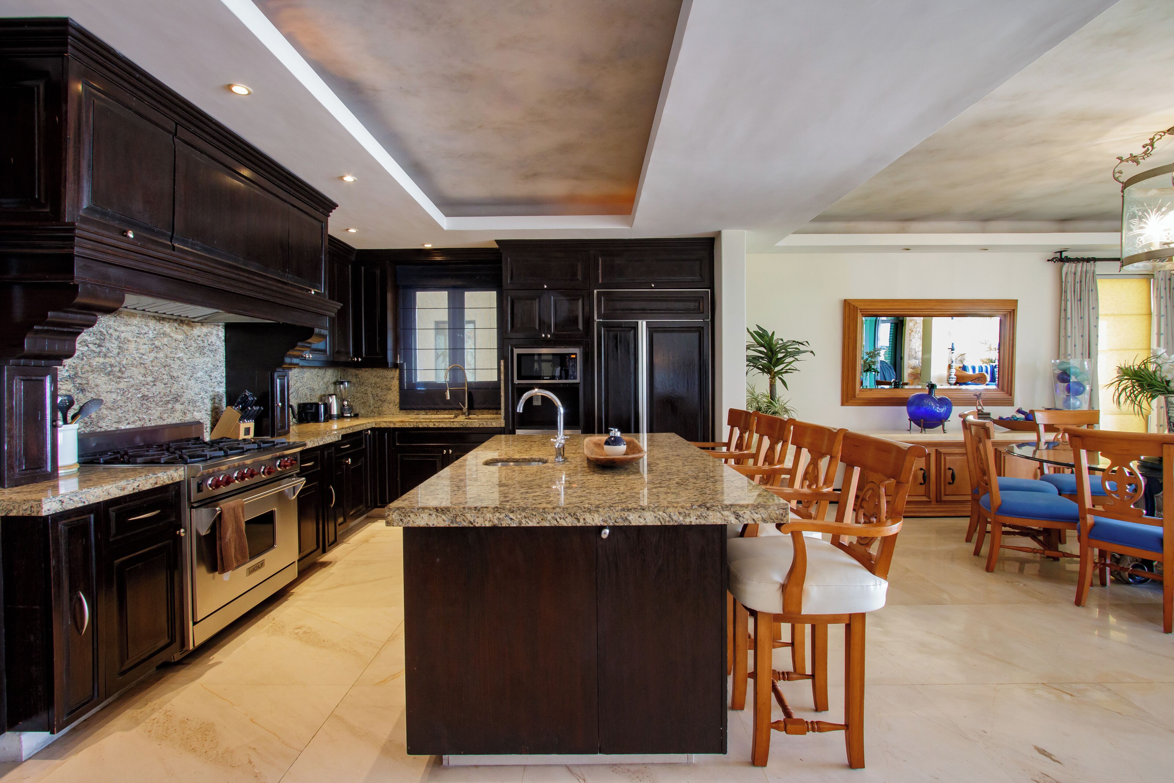 A modern kitchen with dark wood cabinets, granite countertops, stainless steel appliances, and a central island with bar stools.