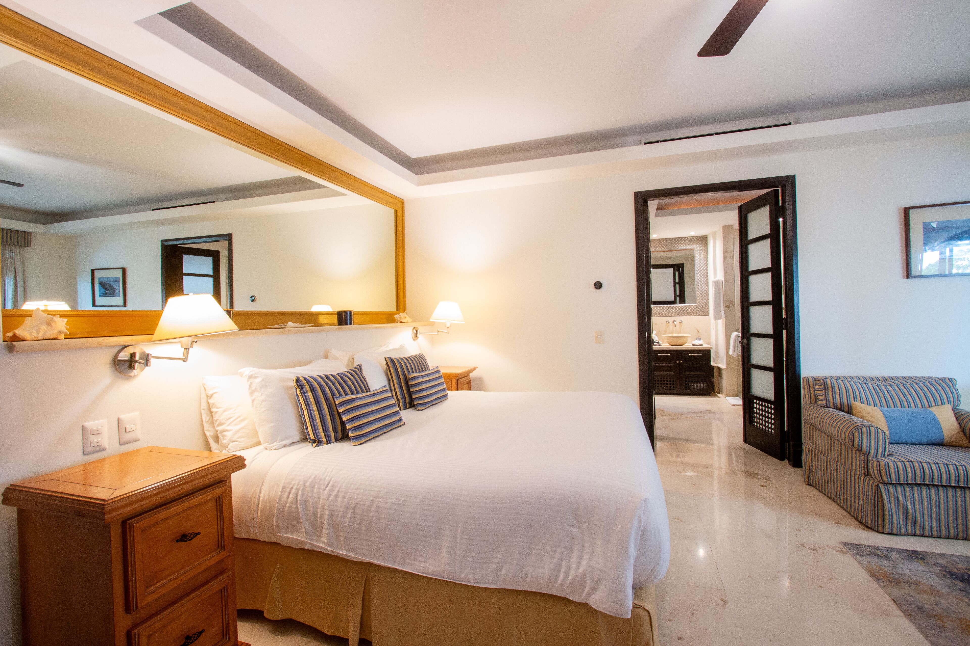 Habitación de hotel con una cama grande, lámparas de noche, una mesita de madera y un sofá a rayas.