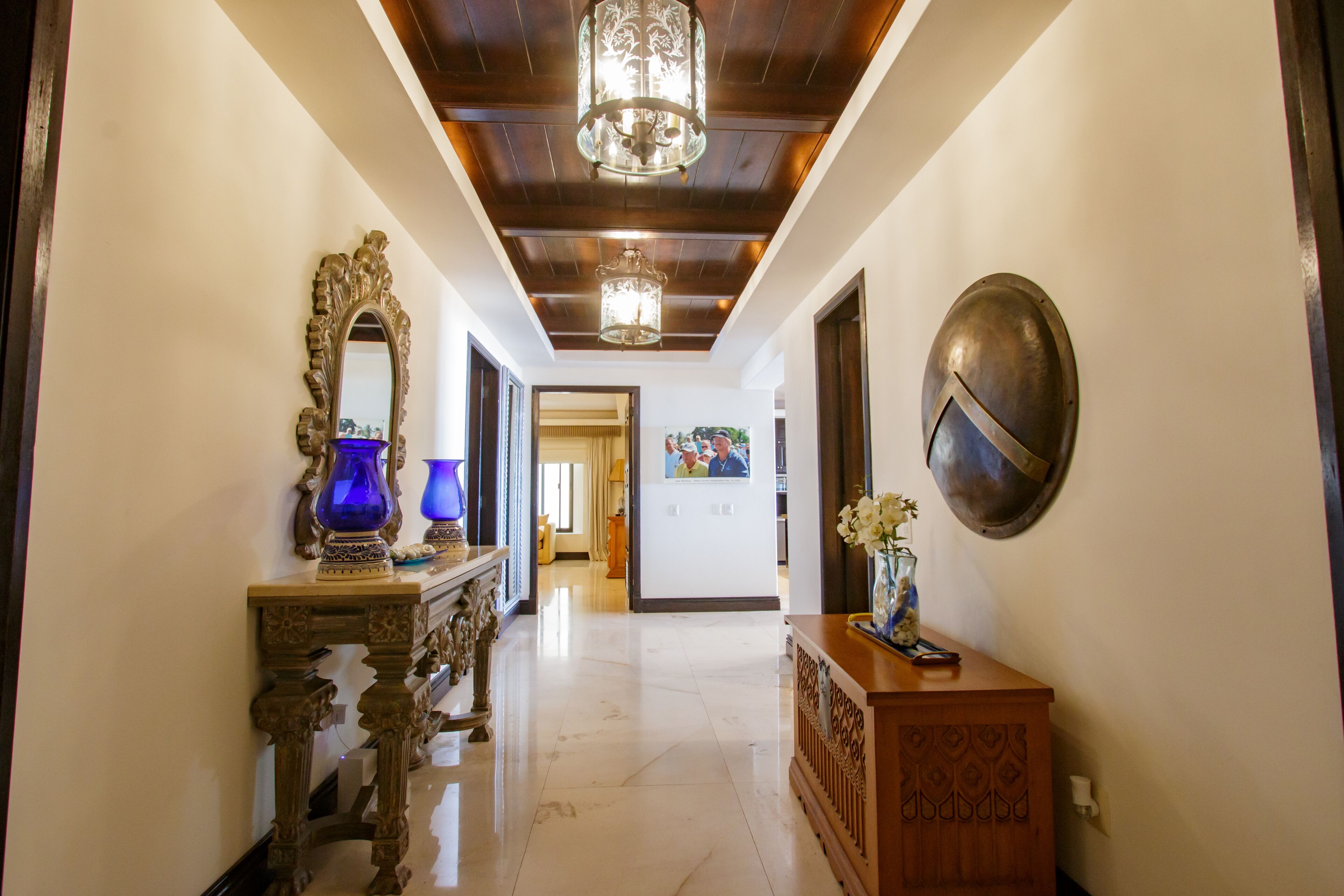 A hallway with a wooden ceiling, a chandelier, a mirror, and a decorative vase.