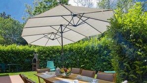 Une terrasse extérieure avec une table en bois mise pour le thé, entourée de chaises, et protégée par un grand parasol.