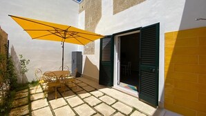 A patio with a table and chairs under a yellow umbrella, a door with green shutters, and a small white object on the ground. - Cosy apartment for 2 guests with A/C, WIFI, TV and pets allowed (Vernole)