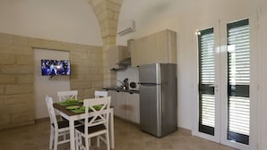 A compact kitchen with a built-in refrigerator, a dining table with chairs, a flat-screen TV mounted on the wall, and a stone wall. - Cosy apartment for 2 guests with A/C, WIFI, TV and pets allowed (Vernole)