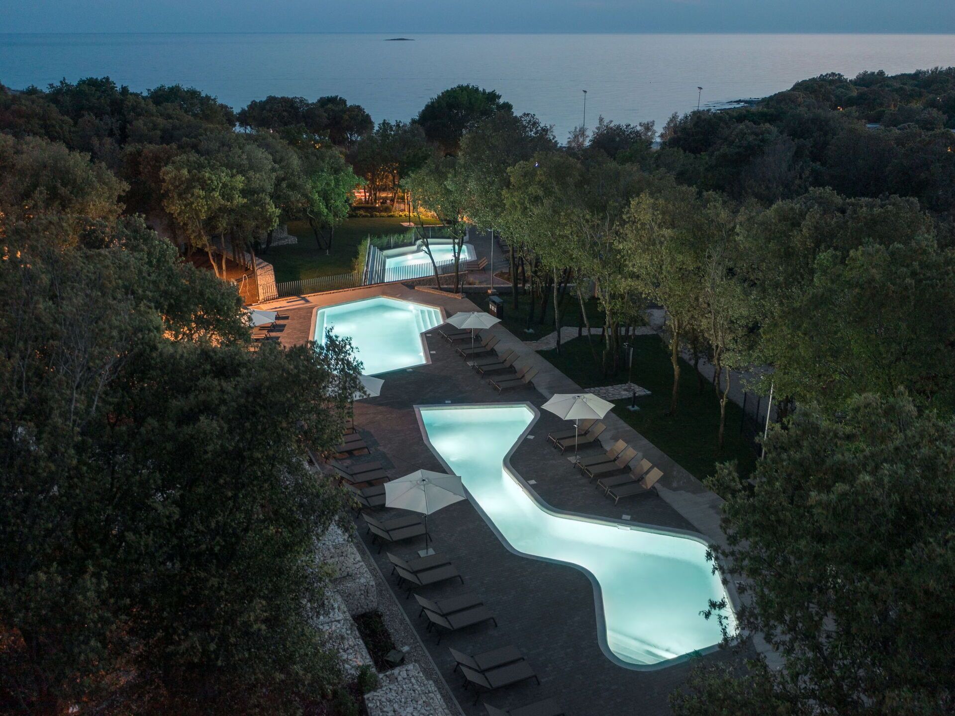 An aerial view of a resort with multiple swimming pools, lounge areas, and a view of the sea.