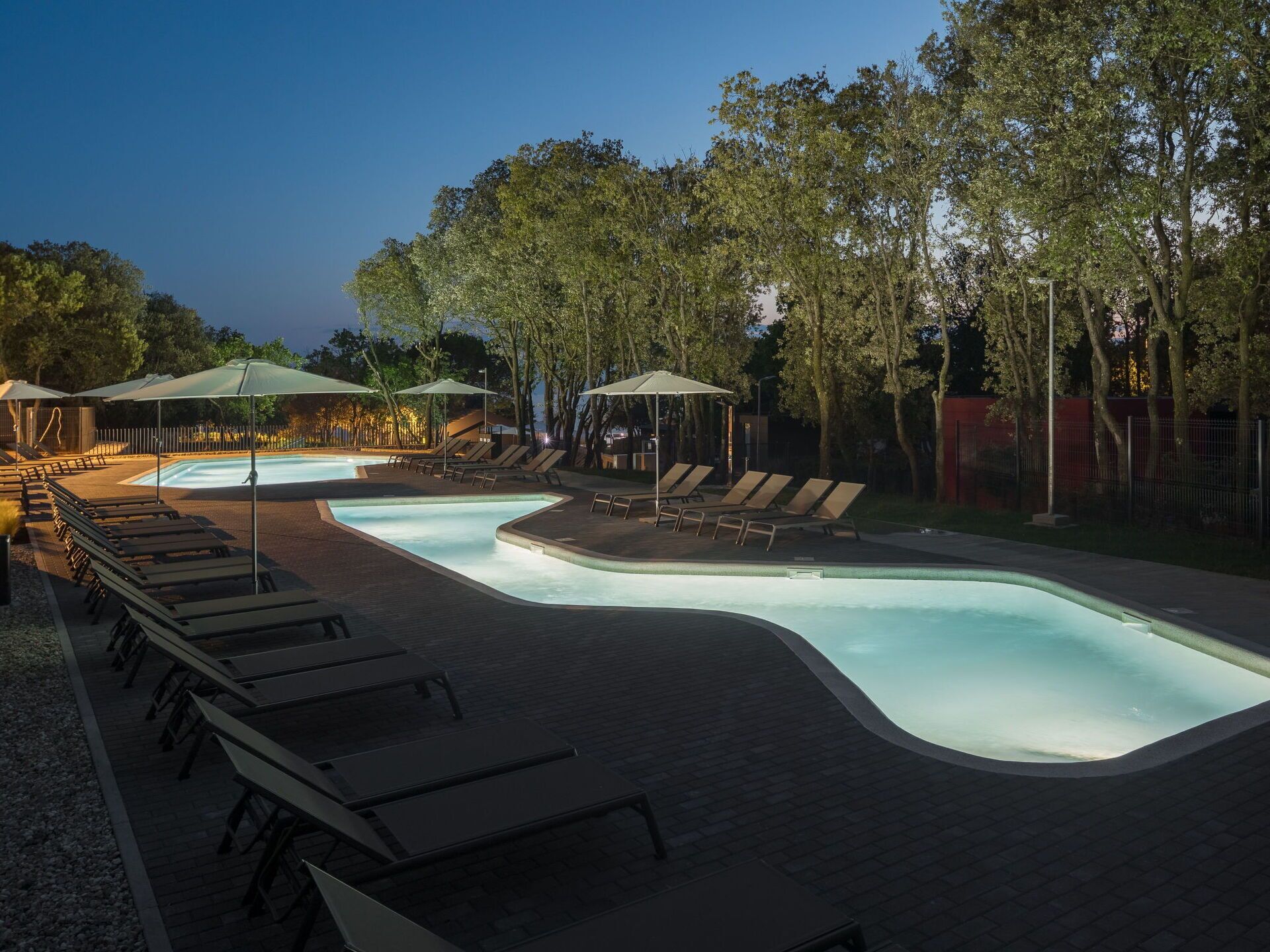 A swimming pool with lounge chairs and umbrellas, surrounded by trees.