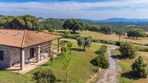 A stone house with a tiled roof, a patio with outdoor furniture, and a view of a rural landscape with trees and hills.