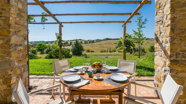 A wooden table set for four with a view of a green landscape through stone walls.