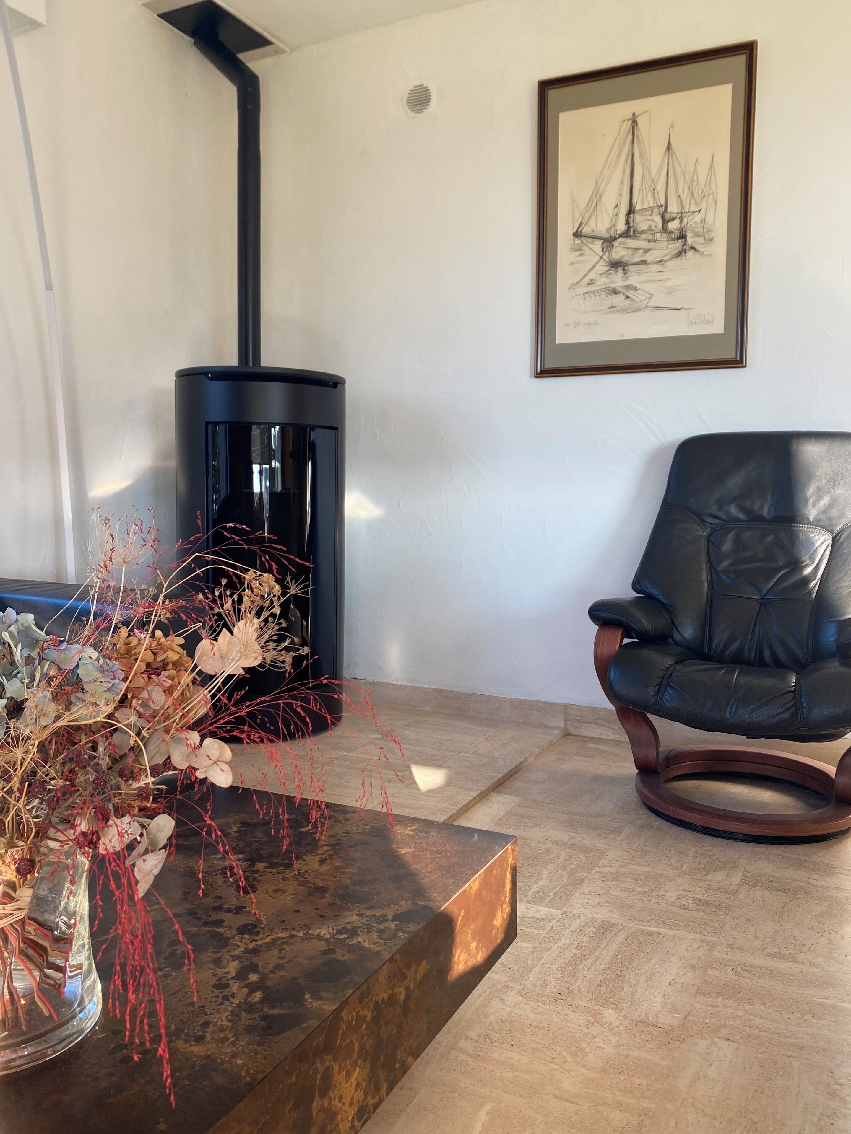 Un salon avec une cheminée, un tableau encadré, un fauteuil en cuir et un vase décoratif.