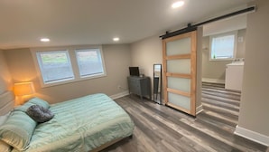 Un dormitorio con cama, cómoda, televisor y puerta corredera que da a un lavadero.