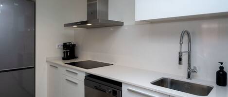 A modern kitchen with a stainless steel refrigerator, a dishwasher, a coffee machine, and a sink with a flexible faucet.