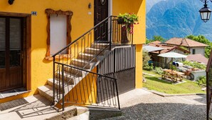 Un edificio amarillo con puerta de madera, una escalera con barandillas negras y vistas a montañas al fondo.