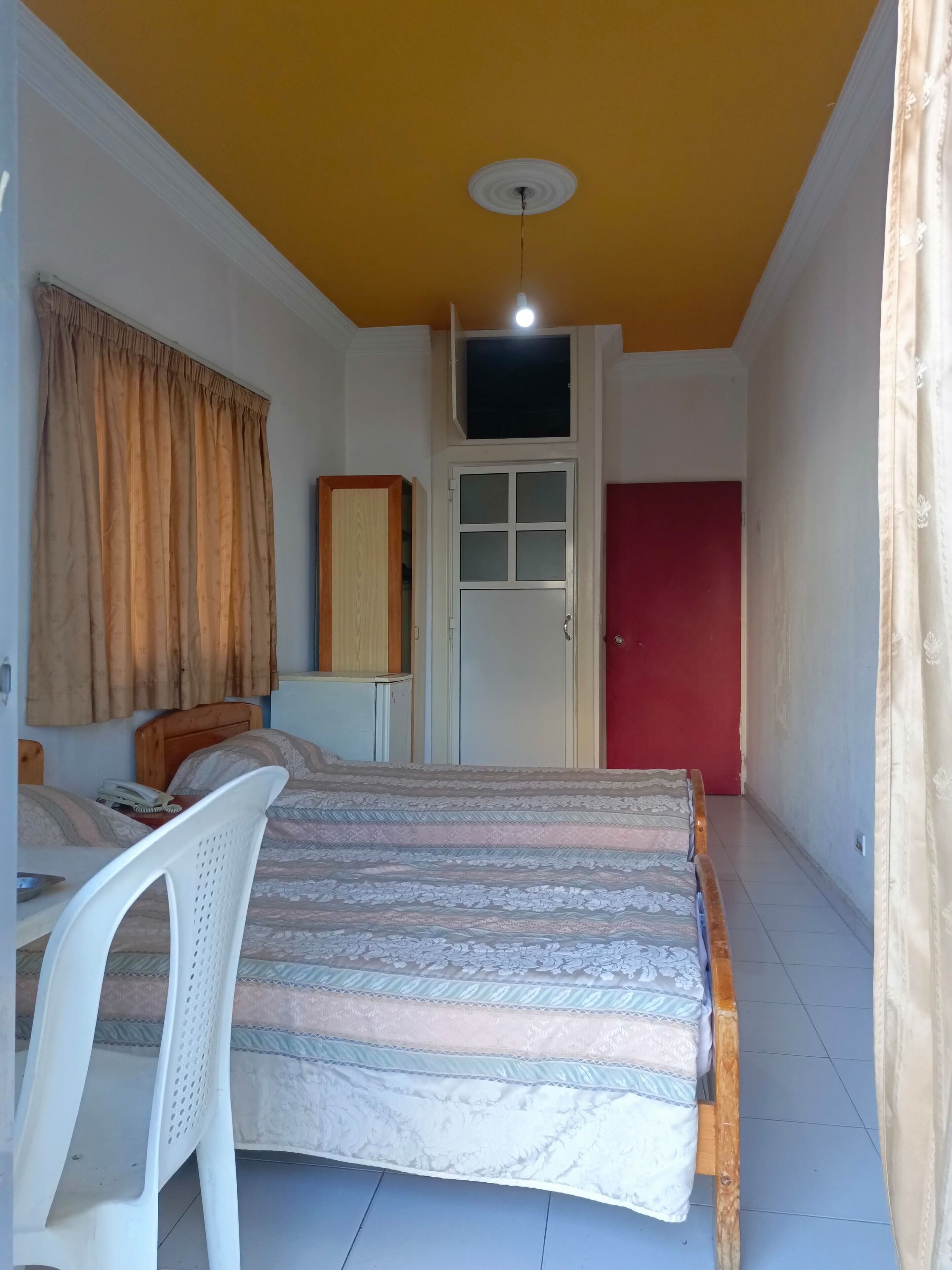 A bedroom with a bed, a chair, a wardrobe, a door, and a ceiling light.