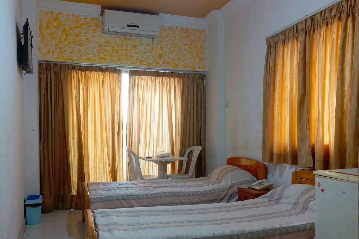 A room with two beds, a small table, a chair, a TV, and an air conditioner.